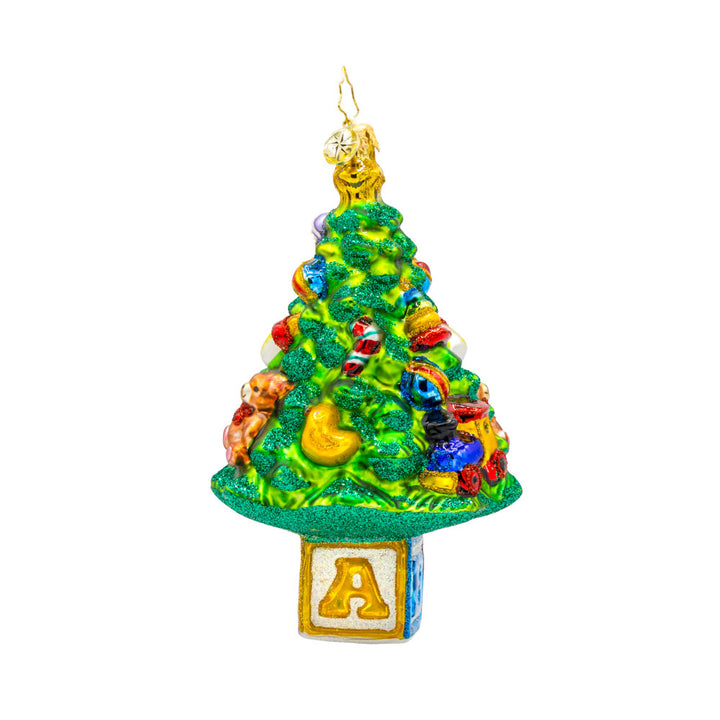 Bundle of Joy Spruce ornament. This piece features a decorated Christmas tree and a collection of baby-themed toys. View of left side.