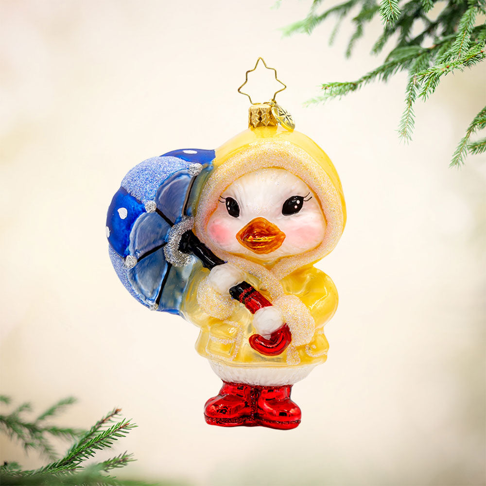Rainy Day Duckling ornament. Dressed in a tiny, vibrant raincoat and rain boots, blue umbrella in tow. View of front.