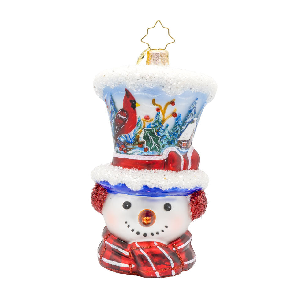Snowy and the Cardinals ornament. This snowman ornament features a hand-painted winter scene, complete with a cozy cabin, a vibrant cardinal, and a snowy landscape. He wears a festive hat, topped with a snowy peak, sparkling glitter muffs and satin scarf. View of front. 