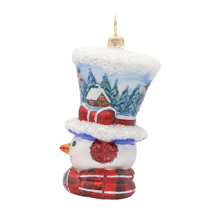 Snowy and the Cardinals ornament. This snowman ornament features a hand-painted winter scene, complete with a cozy cabin, a vibrant cardinal, and a snowy landscape. He wears a festive hat, topped with a snowy peak, sparkling glitter muffs and satin scarf. View of right side.