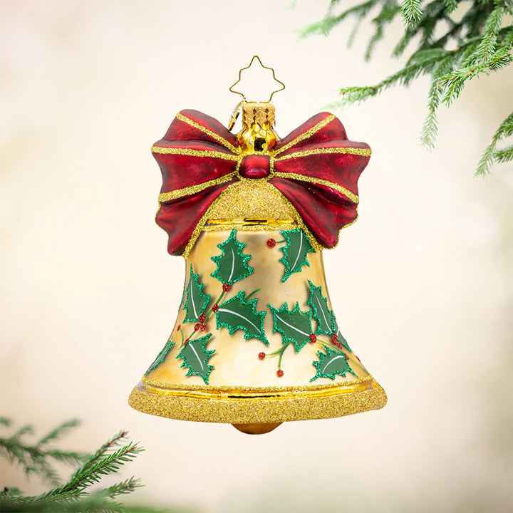 Bell Bliss ornament. A glittery gold bell donned with a red ribbon and hand-painted holly. View of front. 