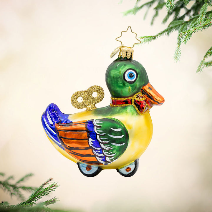 Dapper Duckling ornament. This wind-up duck dons' shiny green feathers, sparkling eyes, and a dapper red bow. View of front. 