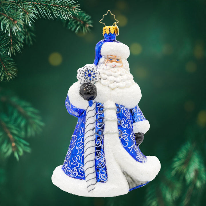 Chinoiserie Santa Charm ornament. Donning a blue satin gown adorned with intricate floral patterns, silver glitter ties, and deep blue gems. View of front.
