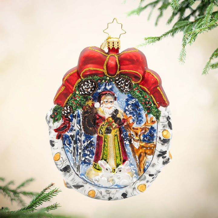 Winter Wonderland Wanderer ornament. Santa and his furry friends explore a snowy wonderland. This scene is framed by a wreath. View of front. 