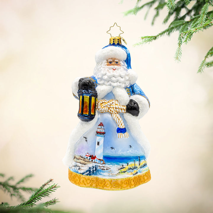 Coastal Claus ornament. Santa dons a blue robe with hand painted lighthouse scene. View of front.