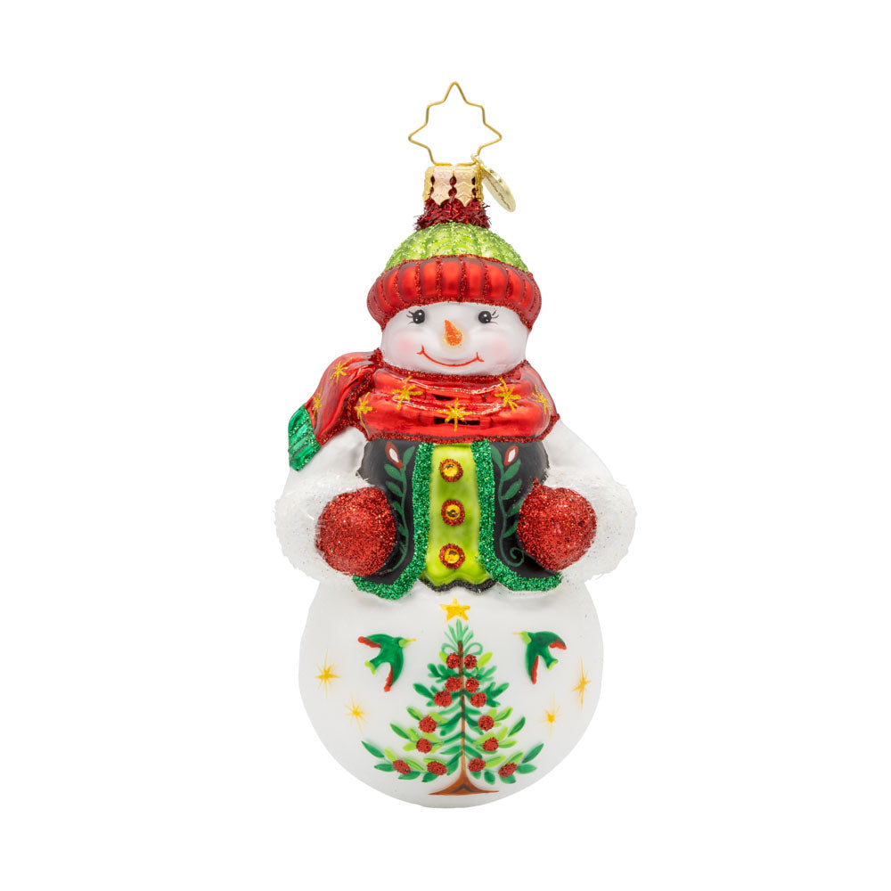 Festive Folk Flair ornament. Dressed in a cozy vest with hand-painted folk-art designs and a cheerful pom-pom hat. His glittering gloves and shining scarf bring the sparkle, while a Christmas tree adorned with stars and berries completes his festive look. View of front. 