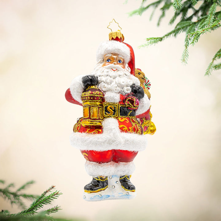 A Clause to Celebrate ornament. With his festive lantern, sparkling eyes, and a cuddly teddy bear by his side. He's dressed in his traditional red suit and hat. View of front. 