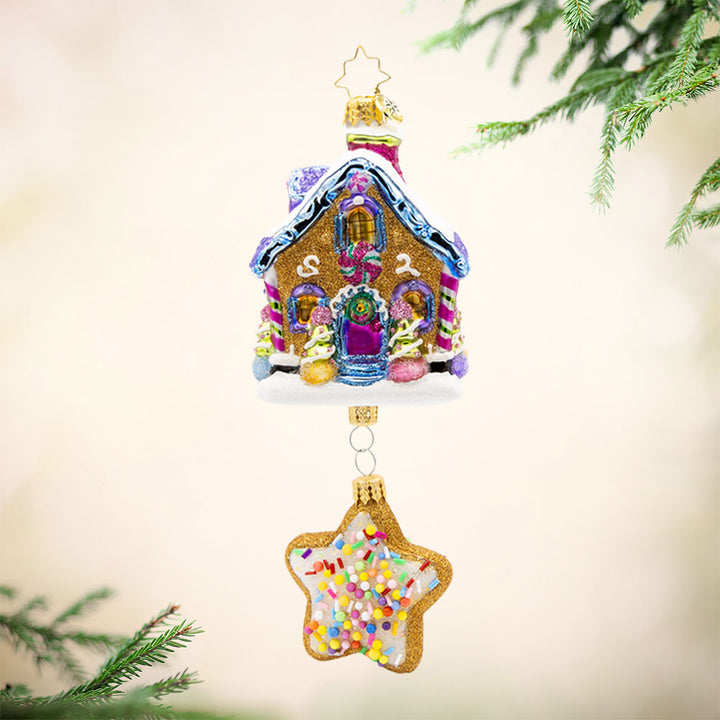 Sweet Beginnings ornament. A gingerbread house decorated in vibrant colors and candy. A gingerbread star cookie covered in sprinkles hangs below. View of front. 