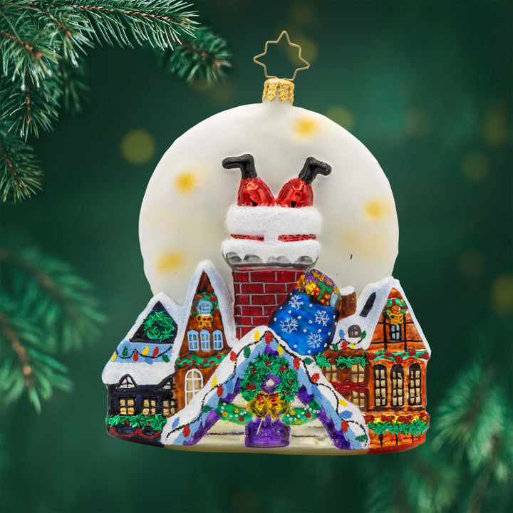 Santa's Moonlight Mischief ornament. Santa goes headfirst down a chimney a set a scene of festive homes lit by a large moon. View of front. 
