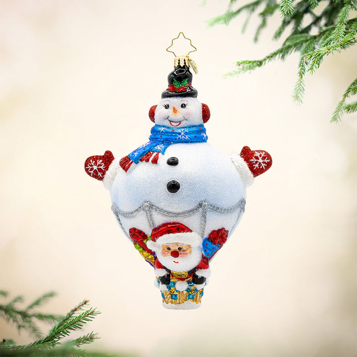Up, Up, and Snowy ornament. This charming piece features a friendly snowman hot-air balloon, and a jolly Santa Claus ready to embark on a festive flight. View of front.