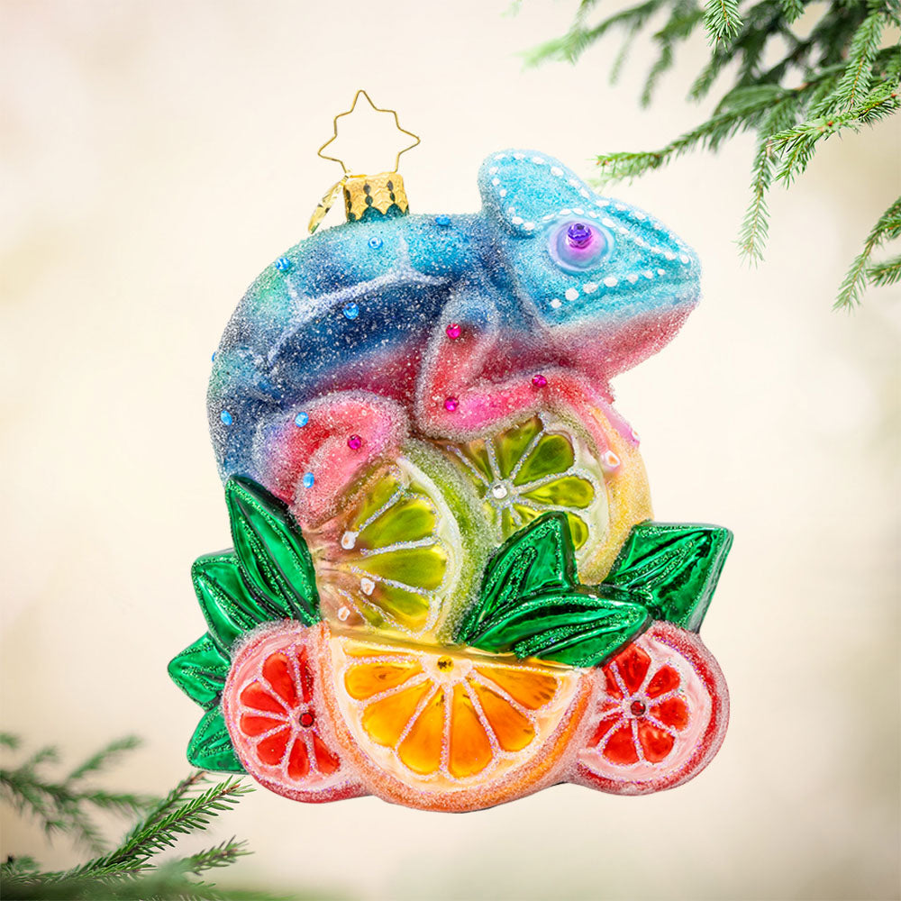 Camouflage Cutie ornament. A chameleon is perched on a vibrant pile of fruit. View of left side.