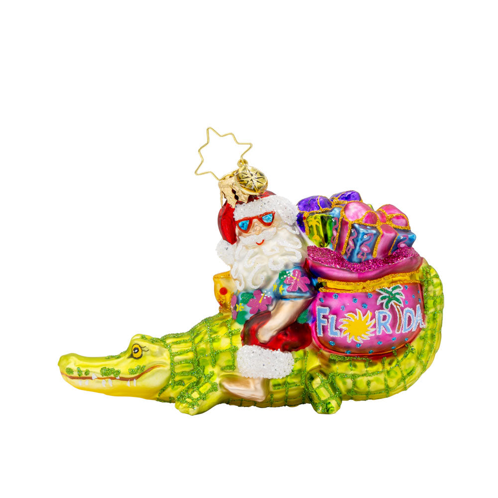Sunshine State Gator ornament. Santa is trading in his sleigh for a gator and enjoying a tropical cocktail. "Florida" is written on gift sack. View of front.