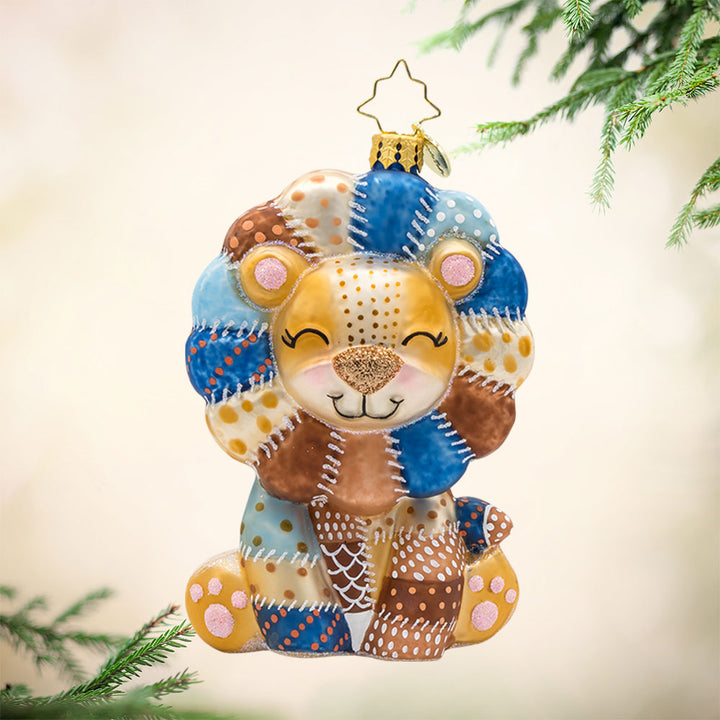 Patchy Paws ornament. This lion is made from beautifully detailed patches and topped with pink glitter accents. View of front. 