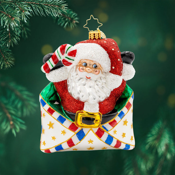 Letters To Santa ornament. Santa is featured here popping out of an envelope covered in gold stars, with a candy cane in his hand. View of front.