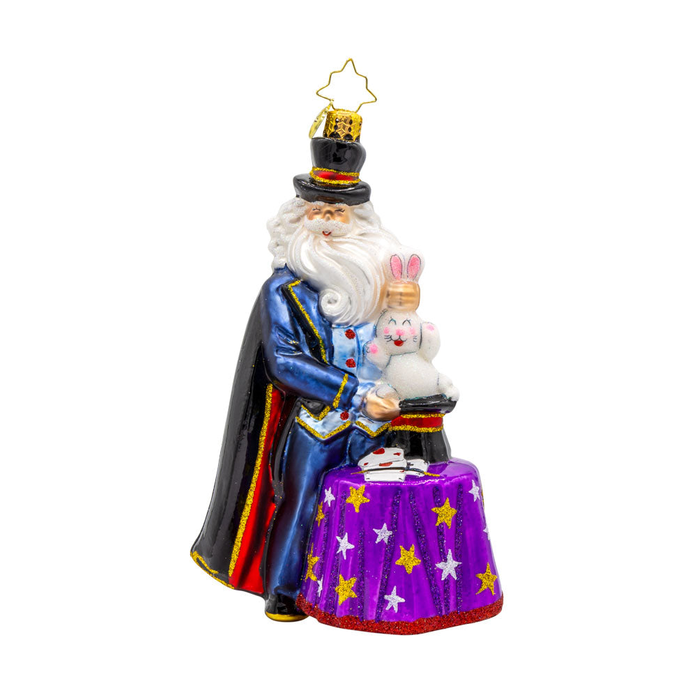 The Merry Magician ornament. Santa features a fluffy beard and cape as he pulls a rabbit out of his sparkling hat. View of front. 