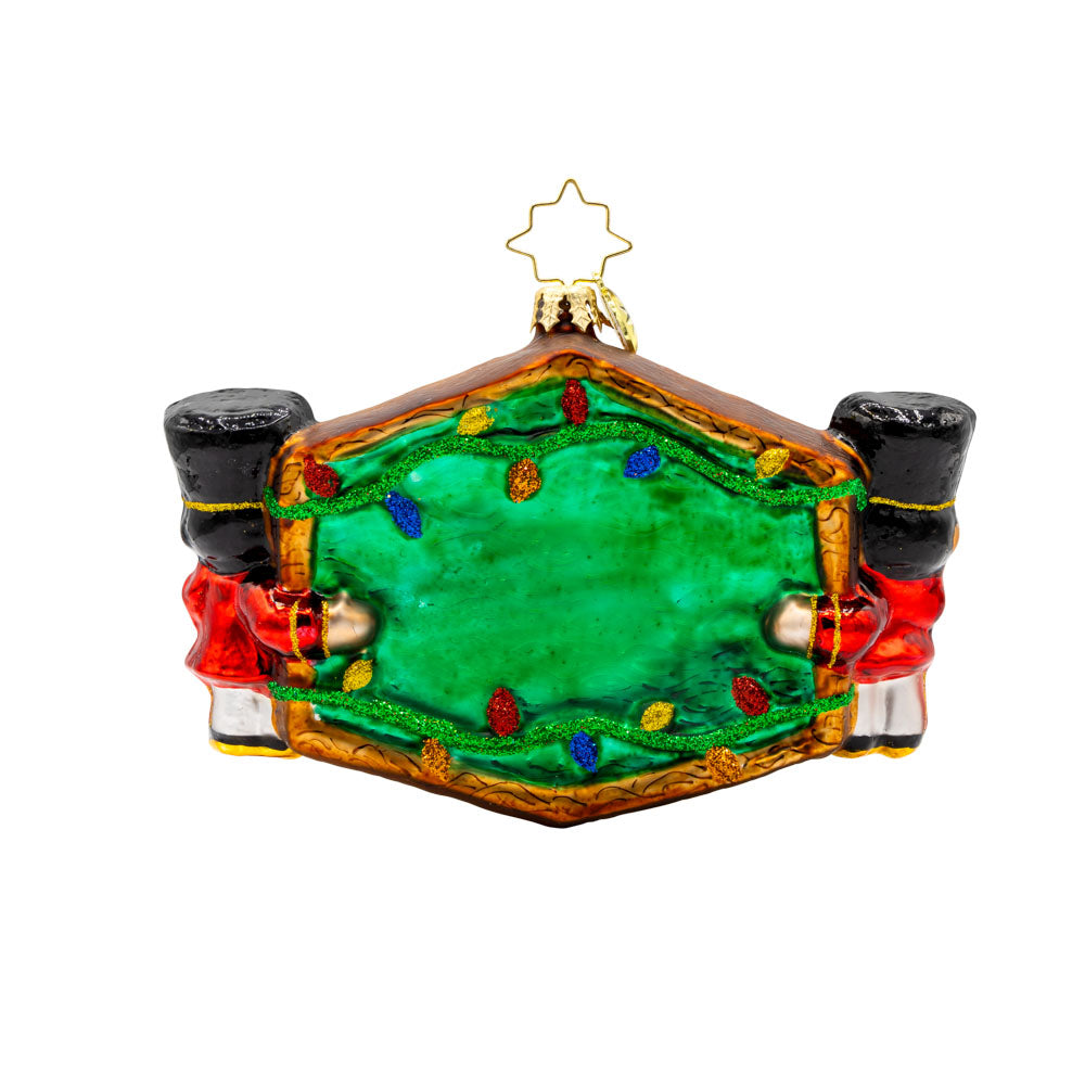 Toyland Sentinels ornament. Two toy soldiers hold up a "Santa's Toy Shop" sign, with their shiny uniforms, festive hats, and sparkling eyes. View of back.