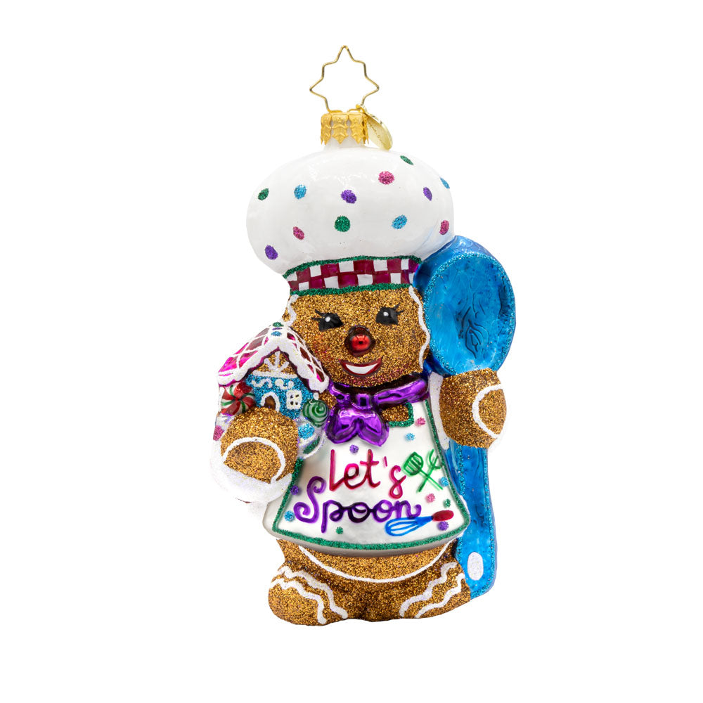 Spoonful of Sweetness ornament. This gingerbread man is wearing a festive chef's outfit, spoon in hand, and gingerbread house in the other. View of front. 