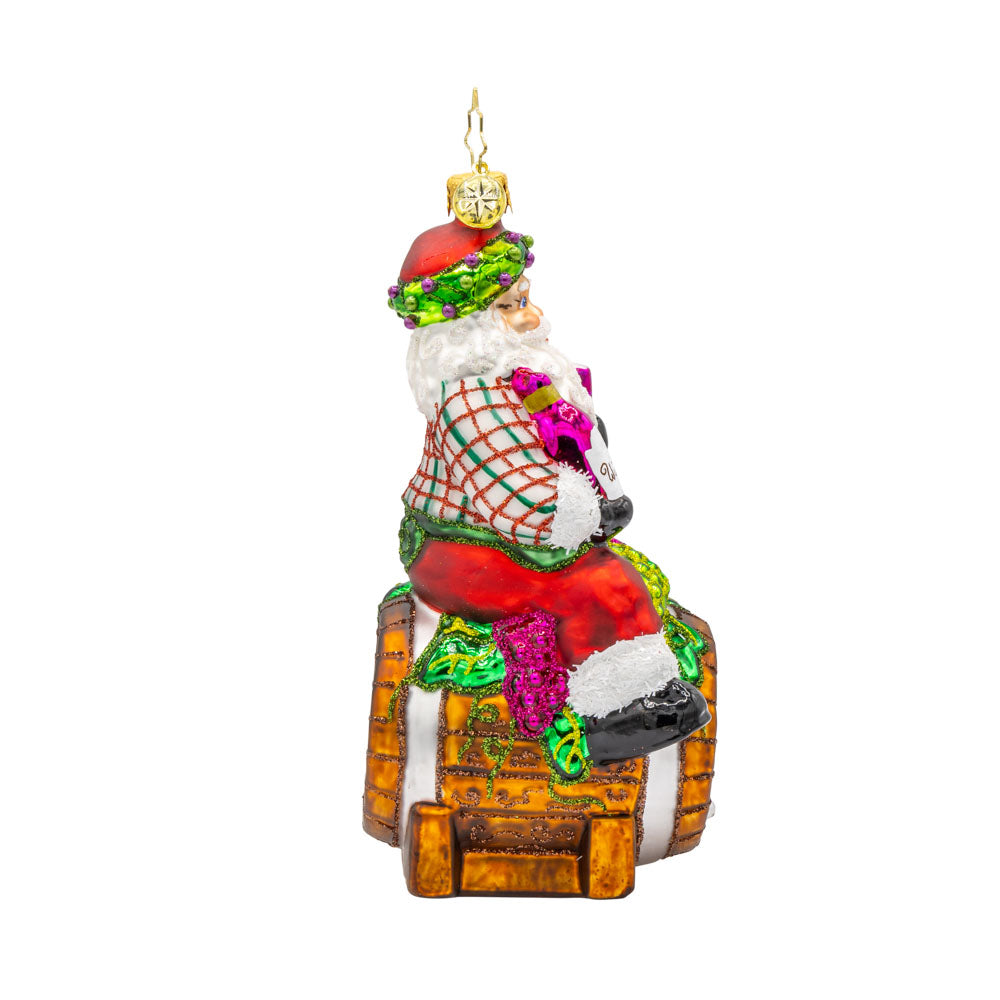 I Believe in Wine Santa ornament. Santa enjoys a glass of wine perched on a barrel. View of left side.