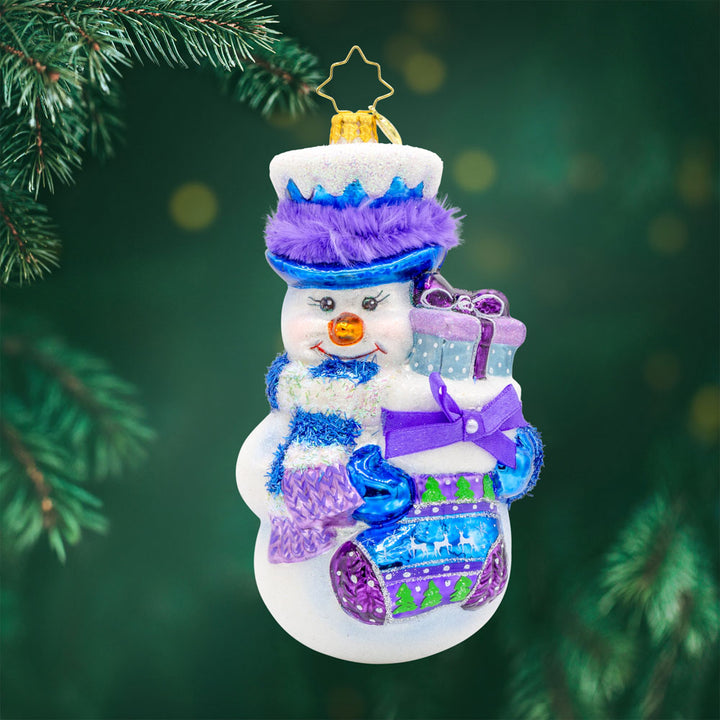 Snowy Stocking Surprise ornament. This snowman features an oversized stocking in festive colors of blue and purple. View of front. 