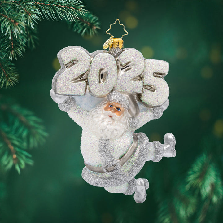 Oh, Shiny Night Ornament! Santa is shining bright, ready to spread holiday cheer. Dressed in a shimmering silver suit and a sparkling hat. "2025" is held above his head in similar colors. View of front. 