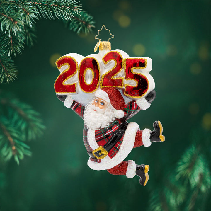 Tartan Time For Fun Ornament. Santa is dressed in a plaid suit, complete with a shiny hat, mittens, and a touch of glitter. "2025" is held above his head in similar colors. View of front. 
