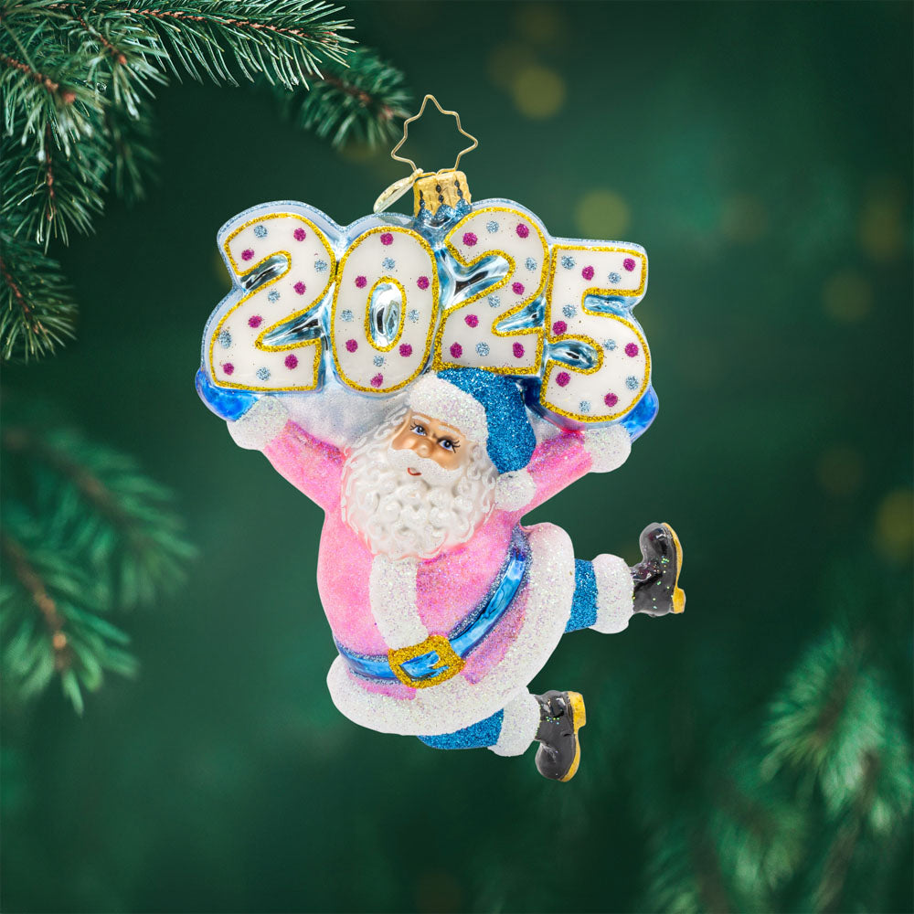 Jingle Bell Jamboree Ornament. Santa's rocking a dazzling outfit with glittering accents and a splash of pink. "2025" is held above his head in similar colors. View of front. 