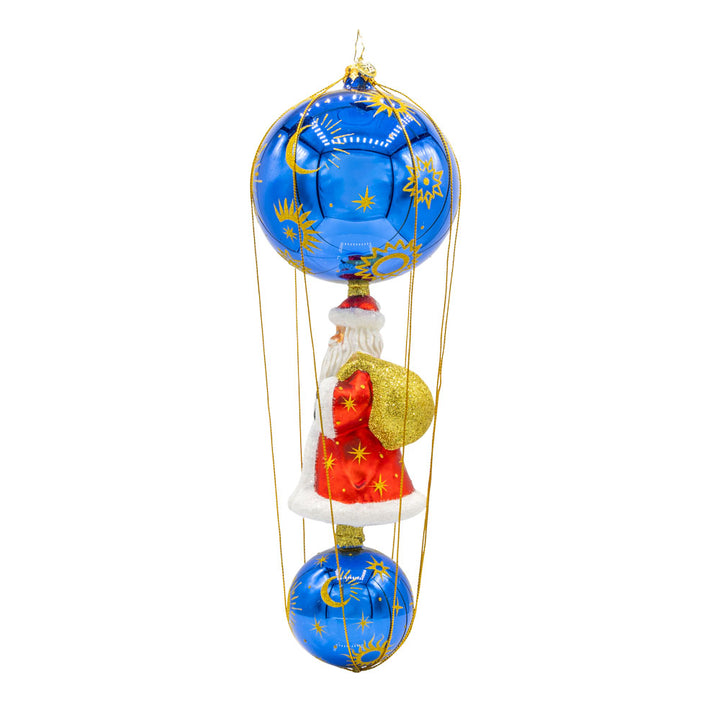 Santa soaring among the stars in a celestial-themed hot air balloon. With its shimmering blue and gold celestial pattern, vibrant red satin Santa, and glittering gift bag, this ornament is a dazzling symbol of holiday wonder and elegance. View of right side.
