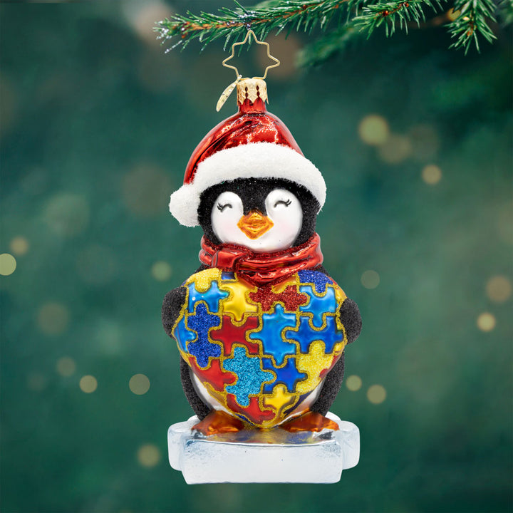 Waddles of Awareness. Ornament of a penguin wearing a red hat and scarf and hold a red, blue, and gold, puzzle heart for the autism community. View of front