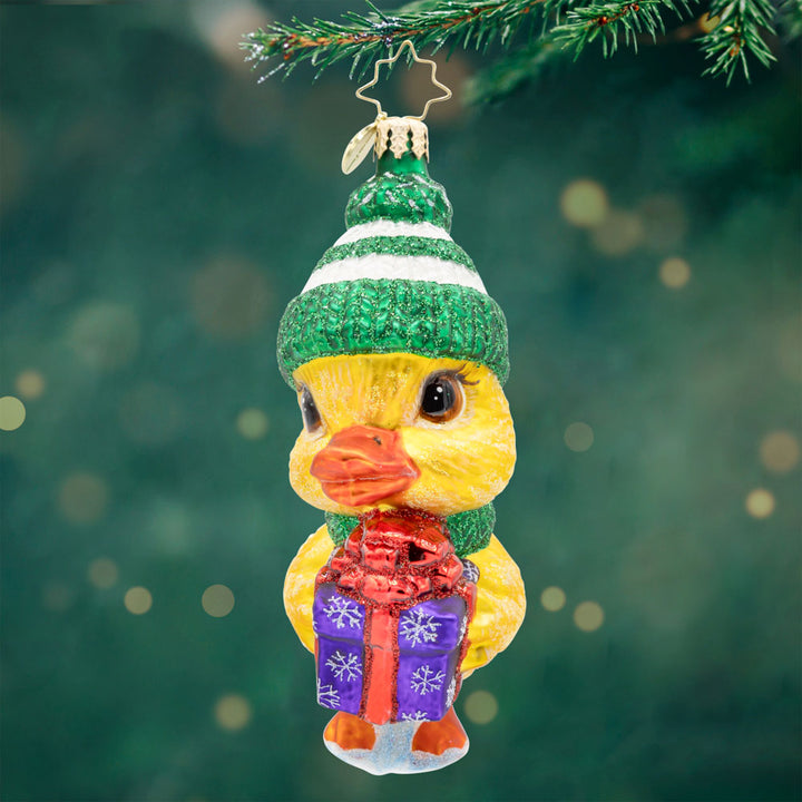 Gift of Courage. Ornament of a yellow duck wearing a green hat and scarf and holding a purple present.