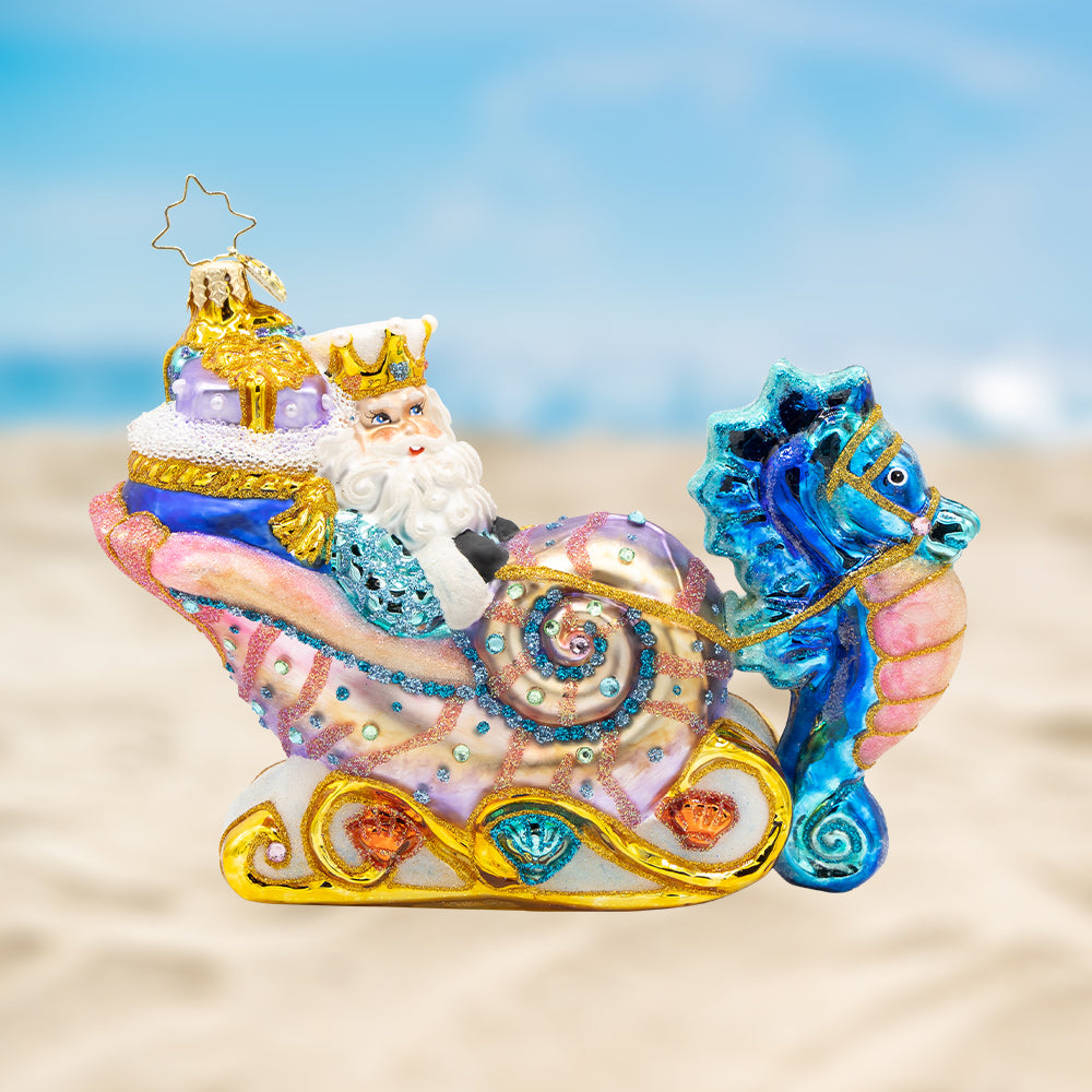 Seashell Sleigh Ride. Ornament of Santa riding in a pink and gold detailed shell shaped sleigh while being pulled by a blue and pink seahorse. View of front