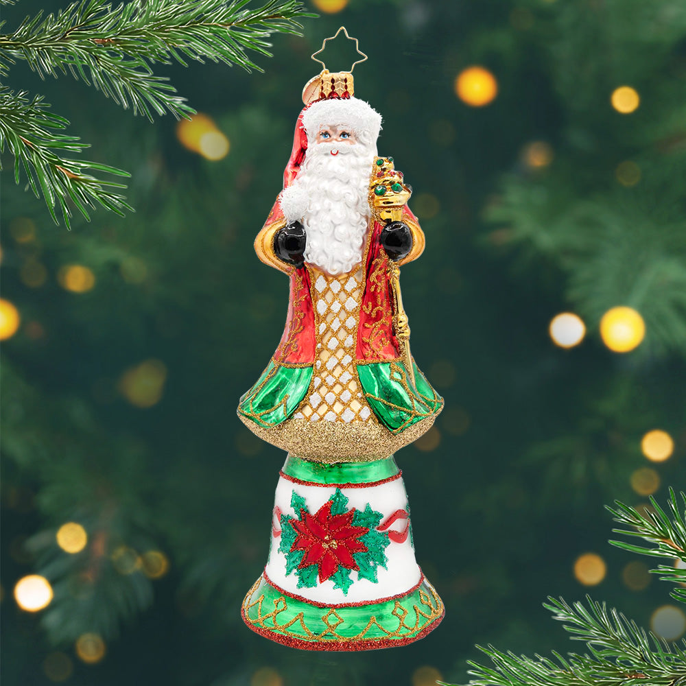 Regal Christmas Chime. Ornament of Santa in a red and green rob with gold details and holding a golden staff, on top of a bell-shaped base with a poinsettia. View of front