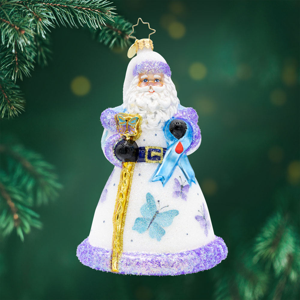 Wings of Hope Santa. ornament of Santa in a white robe with purple trim and flower detailing, while holding a golden staff and a blue ribbon with a blood droplet for diabetes awareness. View of front