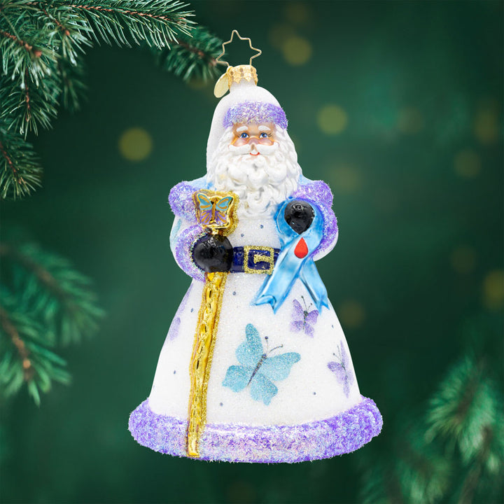 Wings of Hope Santa. ornament of Santa in a white robe with purple trim and flower detailing, while holding a golden staff and a blue ribbon with a blood droplet for diabetes awareness. View of front
