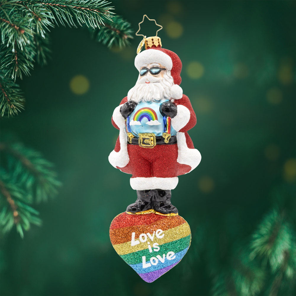 Love Wins Santa. Ornament of Santa in his red suit and a blue shirt with rainbow, with Santa standing on top of a rainbow heart with the phrase "love is love." View of front