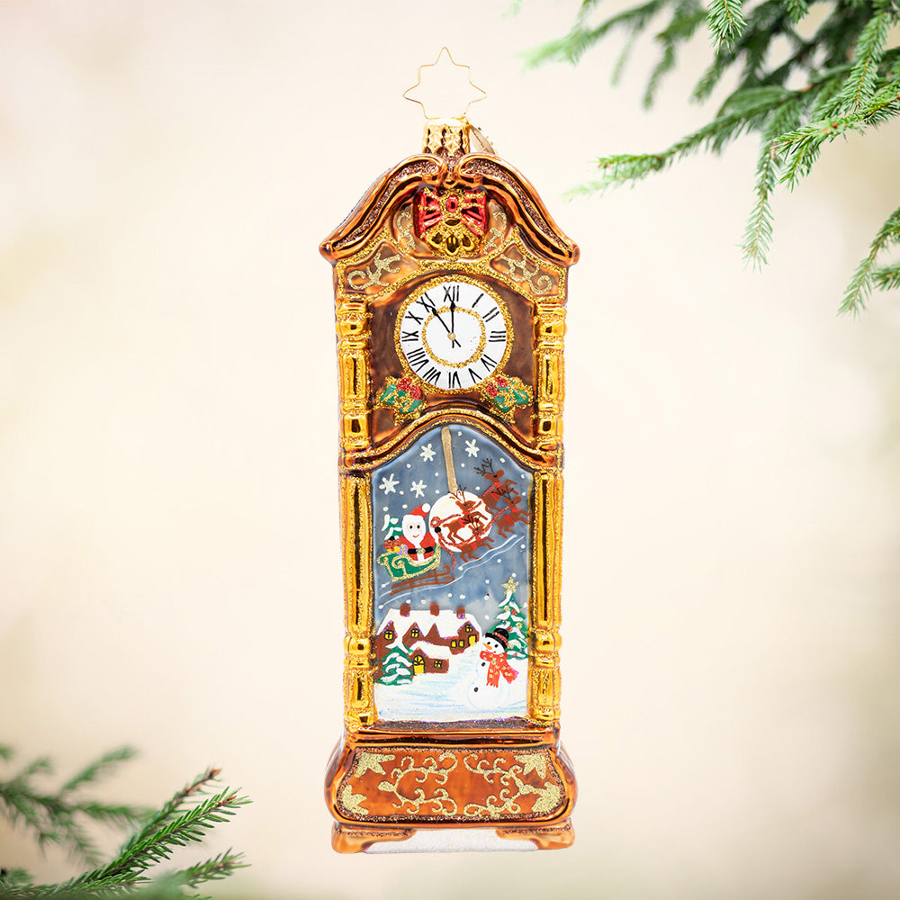 Sleighbells Past Midnight. Ornament of a gold and brown grandfather clock with a scene of Santa arriving to town in his sleigh.