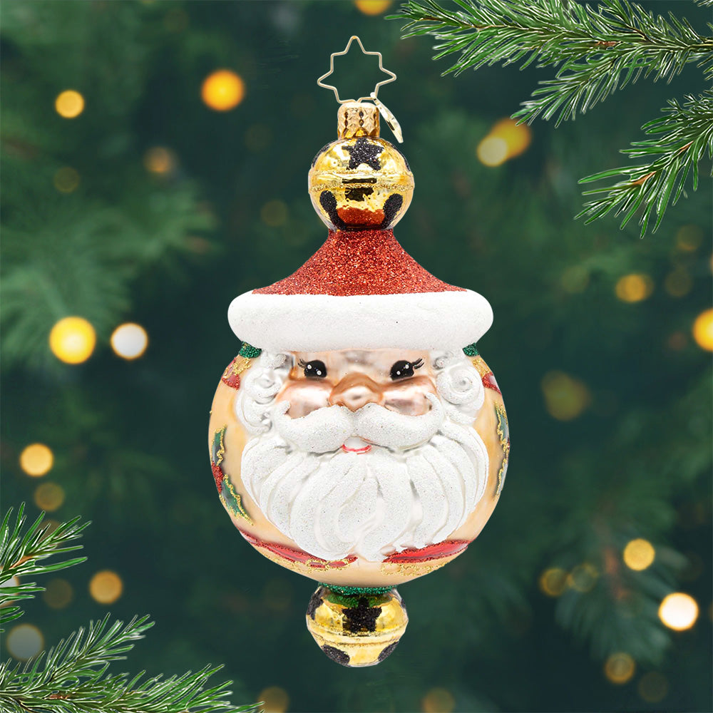 Holly Jingle Joy. Ornament of Santas face with a red hat and brown background and a one golden bell with black stars on top and on the bottom. View of front