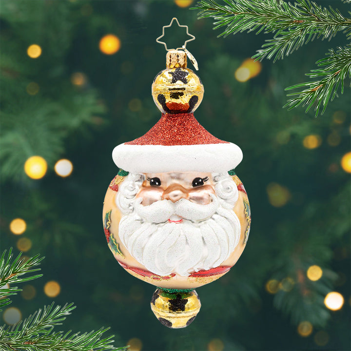 Holly Jingle Joy. Ornament of Santas face with a red hat and brown background and a one golden bell with black stars on top and on the bottom. View of front