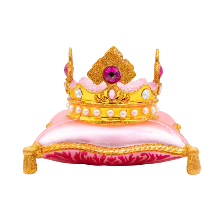 The Crown Jewel. Ornament of a golden crown with white and pink gems on a pink pillow with golden trim. View of front.