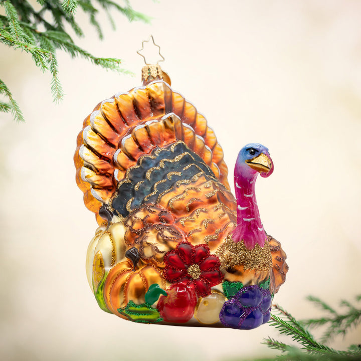 A Grateful Gathering. Ornament of a golden turkey with a pink head, surrounded by pumpkins, grapes, apples, and a ref flower. View of front
