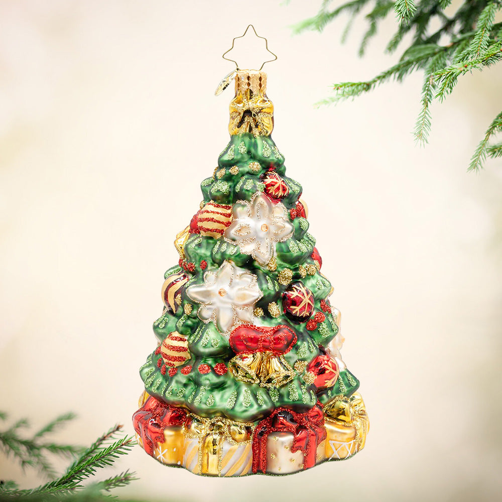 Golden Bloom Fir. Decorated Christmas tree ornament with two white poinsettias, red and ornaments as well as a base full of presents. View of front.