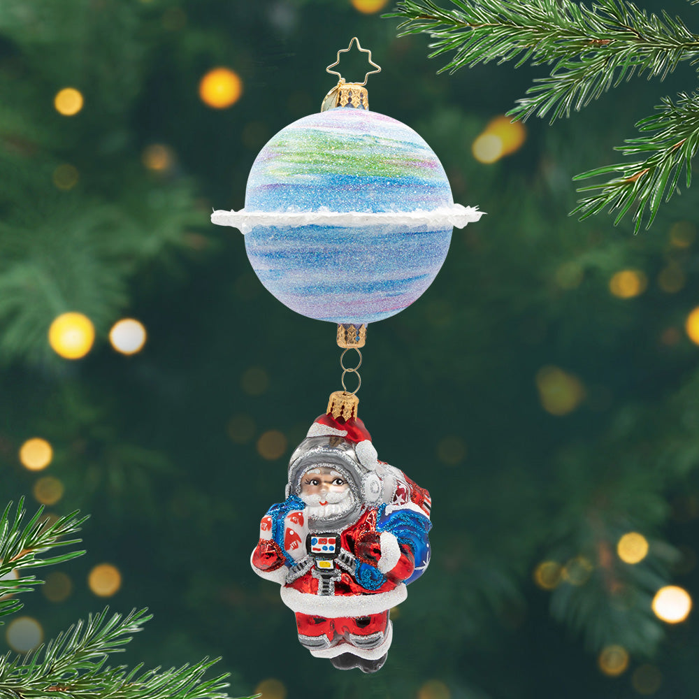 Space Nick. Ornament of Santa in a red astronaut uniform being held by a blue, with hints of green and pink, planet. View or front