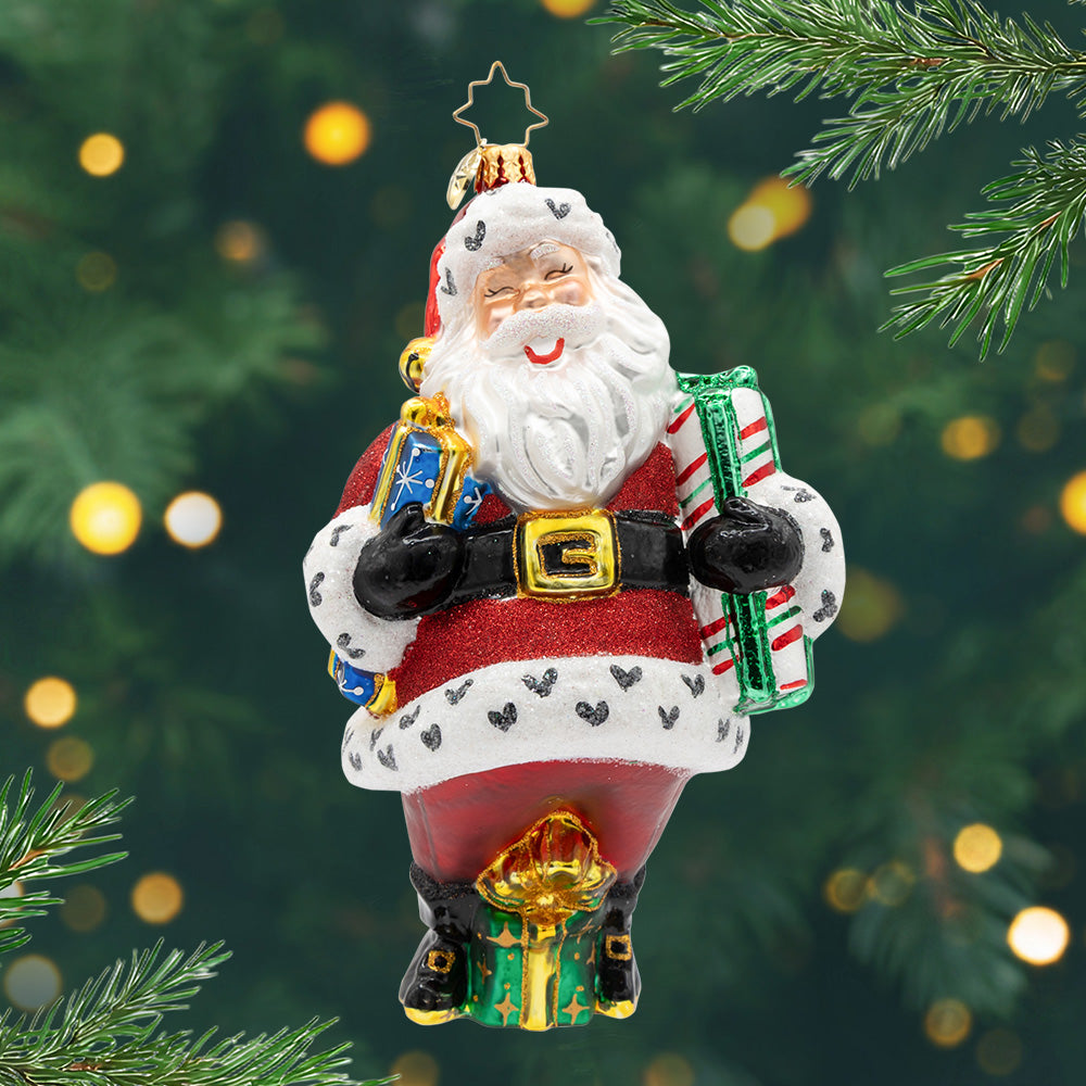 Jingle & Jolly. Ornament of Santa in his classic red suit with black hearts on the trim and holding a blue and striped in each arm and one green one at his feet. View of front