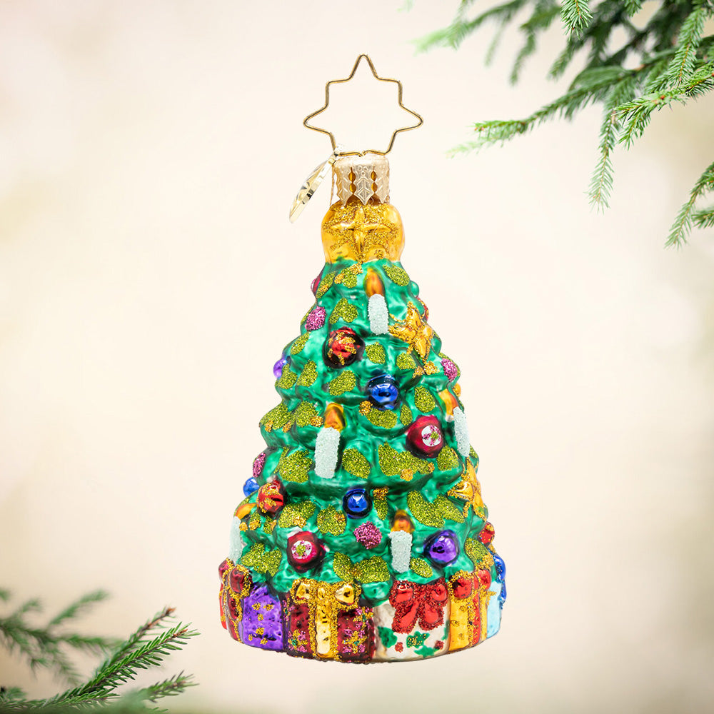 Twinkling Tree Gem. Ornament of a sparkly Christmas tree decorated in red, blue and purple ornaments with gold details and a base full of colorful presents. View of front
