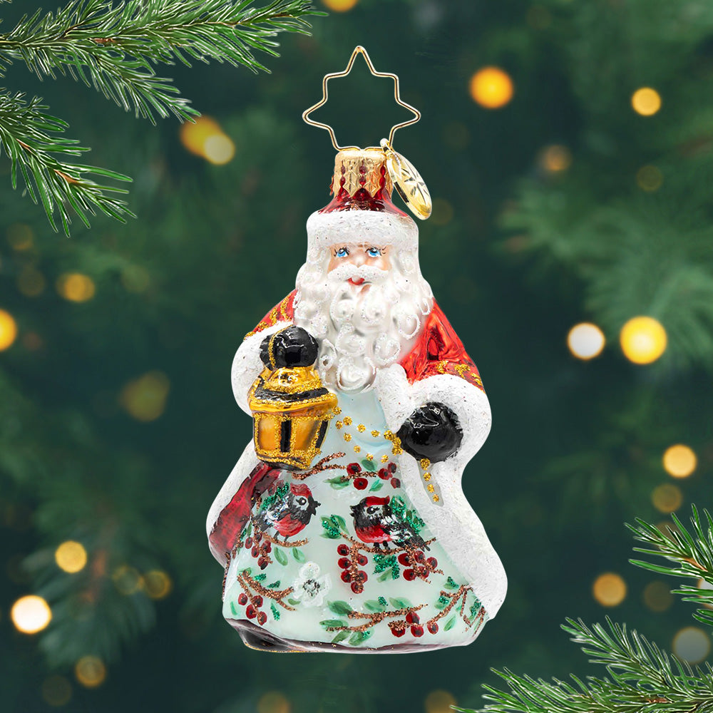 Cardinal Kris Kringle Gem. Ornament of Santa in a red and white robe with a scene of two cardinals on sparkly branches in the front, while Santa holds a gold lantern. View of front.