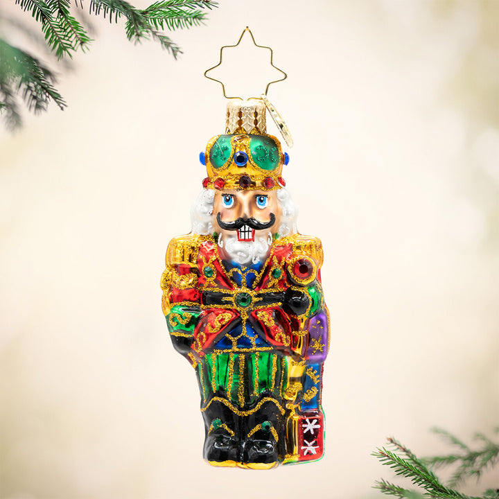 Yuletide Sentinel Gem. Nutcracker ornament dressed in colors of red, blue, and green with gold detailing and a crown. View of front