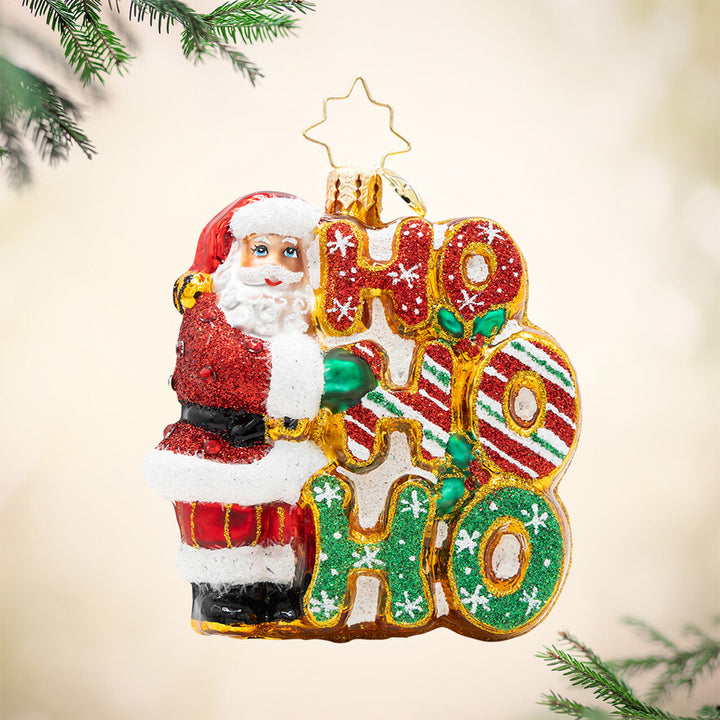 Merry Ho Ho Ho Santa Gem. Ornament of Santa in a sparkly red suit next to the phrase "HO HO HO' which are in different patterns of sparkling colors, red and green. View of front.