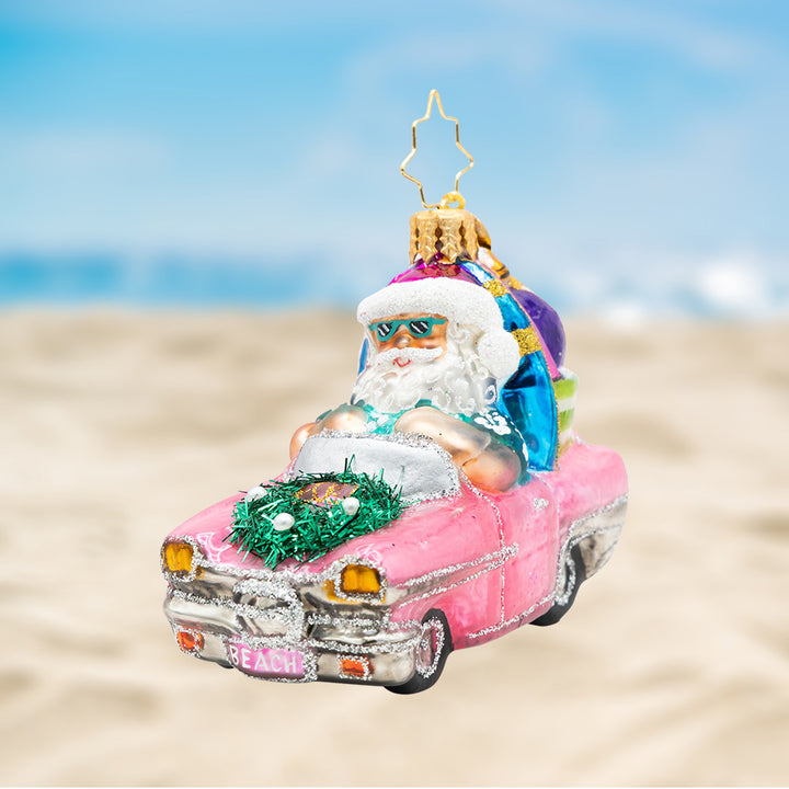 Santa's Coastal Christmas Ride Gem. Ornament of Santa in a pink convertible with a blue surfboard, shades, and shirt. View of front