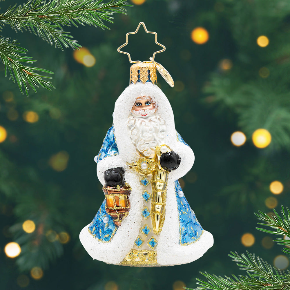 Gilded Grandeur Santa Gem. Santa ornament of him in a blue coat with intricate patterns in sparkling blue and gold, while holding a golden staff and a lantern. View of front
