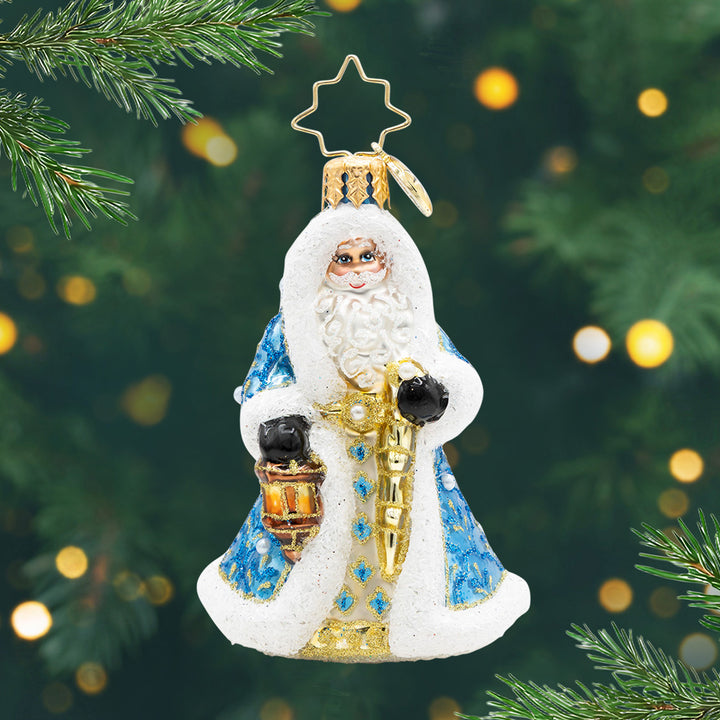 Gilded Grandeur Santa Gem. Santa ornament of him in a blue coat with intricate patterns in sparkling blue and gold, while holding a golden staff and a lantern. View of front