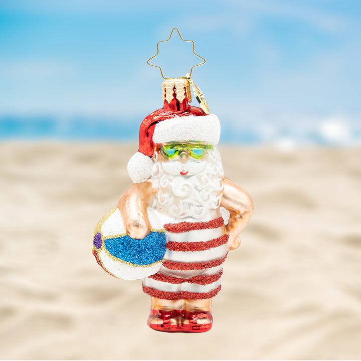 Santa Takes a Dip Gem. Ornament of Santa in a red and white sparkly stripped swim trunks and holding a beachball. View of front.
